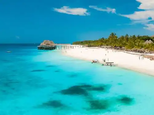 Turquoise ocean with beach hut, white sands and palm trees in Zanzibar.